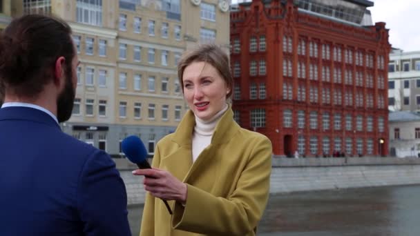 Jovem jornalista atraente está entrevistando um jovem empresário na cidade. Jovem mulher trabalhando como repórter de TV de mídia com homem de negócios . — Vídeo de Stock