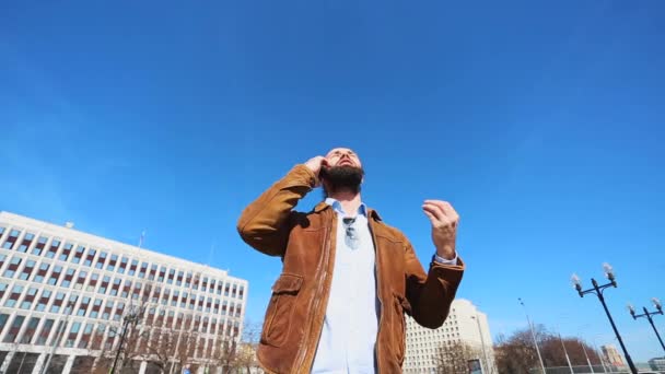 Hombre emocional hablando en un teléfono inteligente y está enojado contra un cielo azul . — Vídeo de stock