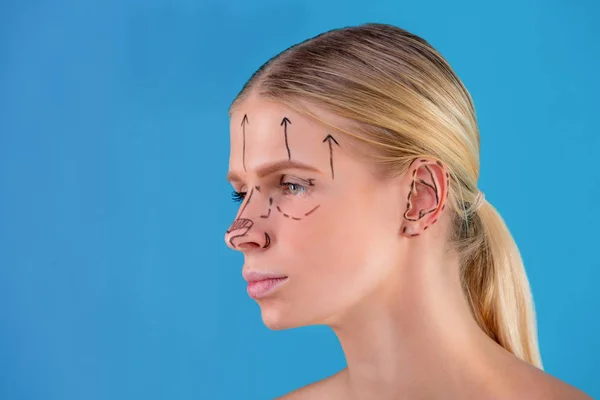 Güzellik uzmanı kadın yüzüne düzeltme çizgileri çizer. Plastik cerrahi operetion önce. Mavi üzerine izole — Stok fotoğraf