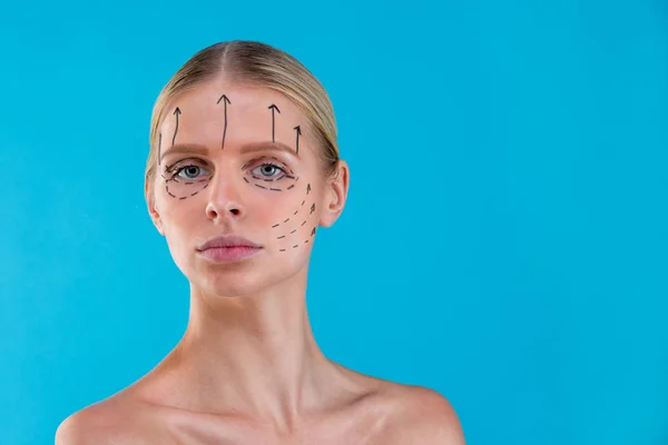 Güzellik uzmanı kadın yüzüne düzeltme çizgileri çizer. Plastik cerrahi operetion önce. Mavi üzerine izole — Stok fotoğraf