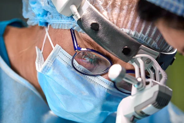 Foto del cirujano en la sala de cirugía. Cirujano en máscara y gafas con faro montado. Retrato cerrado — Foto de Stock