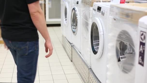 Young man taking clothes out of washing machine in big store. Comic video — 비디오