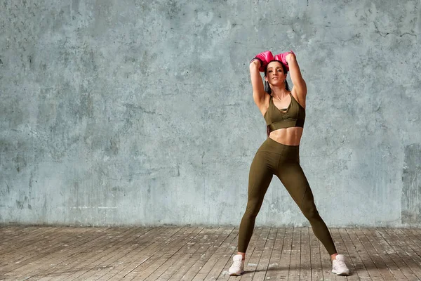 Schöne athletische Mädchen posiert in rosa Boxhandschuhen auf einem grauen Hintergrund. Kopierraum. Konzept Sport, Kampf, Zielerreichung. — Stockfoto