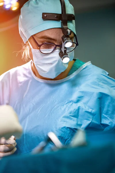 Chirurgien pratiquant une chirurgie en salle d'opération. Chirurgien masqué portant des loupes pendant la procadure médicale . — Photo