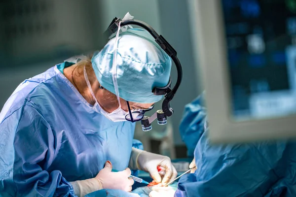 Chirurgien et son assistant pratiquant la chirurgie esthétique en salle d'opération de l'hôpital. Chirurgien masqué portant des loupes pendant la procadure médicale . — Photo