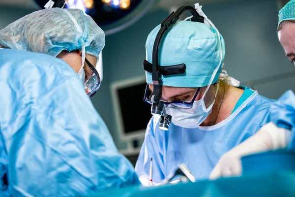 Chirurgien et son assistant pratiquant la chirurgie esthétique en salle d'opération de l'hôpital. Chirurgien masqué portant des loupes pendant la procadure médicale . — Photo