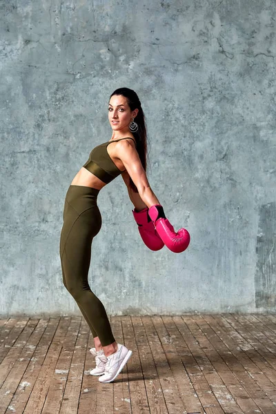 Hermosa chica atlética posando en guantes de boxeo rosa sobre un fondo gris. Copiar espacio. Concepto deporte, lucha, logro de metas . — Foto de Stock