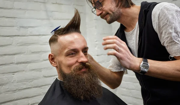 Männliche Friseur macht eine Mohawk-Frisur mit Clipper eines erwachsenen Mannes mit Bart — Stockfoto