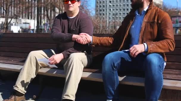 Transfer bribes in the street. A man gives money in an envelope to another man while sitting on the bench in the park — Stock Video