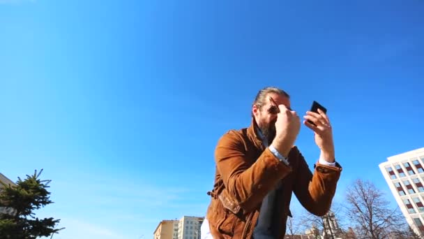 Jovem nervoso falando emocionalmente ao telefone. Cara com barba e óculos nervosamente fala ao telefone — Vídeo de Stock