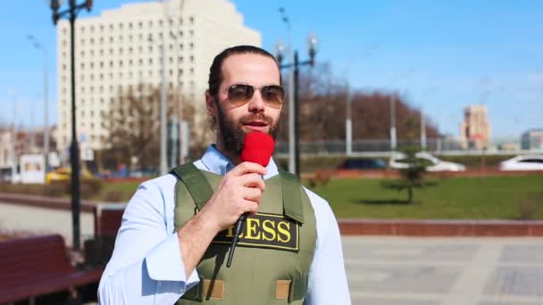 Een succesvolle journalist is een man in een Bulletproof vest met een microfoon in zijn handen, Live op straat, een alarmerend verslag. — Stockvideo