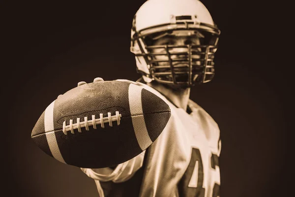 American football player holding the ball in his hands in front of the camera. Concept American football, motivation, black background — Stock Photo, Image