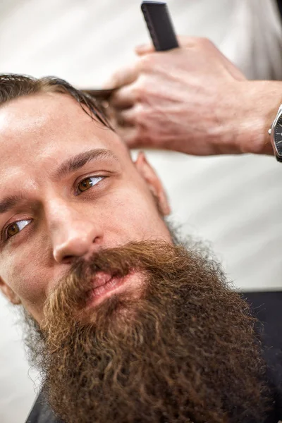 Stylish barber cuts a brutal man with a thick beard.