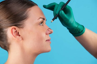 Güzellik uzmanı kadın yüzüne düzeltme çizgileri çizer. Plastik cerrahi operetion önce. Mavi üzerine izole