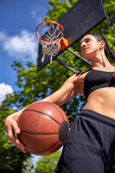 Hermosa chica sexy fitness en ropa deportiva negro con el cuerpo perfecto con pelota de baloncesto en la cancha de baloncesto. Deportes, fitness, concepto de estilo de vida — Foto de Stock