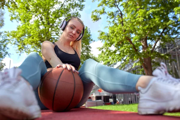 Hermosa chica sexy fitness en ropa deportiva negro con el cuerpo perfecto con pelota de baloncesto en la cancha de baloncesto. Deportes, fitness, concepto de estilo de vida — Foto de Stock