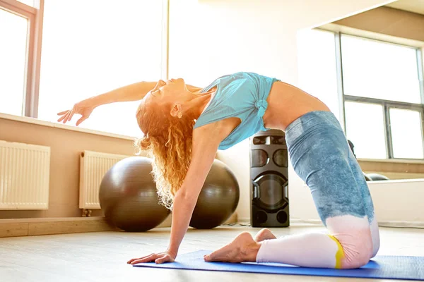 Mujer atractiva joven haciendo yoga en la sala de fitness. Luz natural ambiente . — Foto de Stock