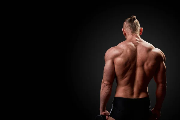 Sport concept. Fitness athlete with perfect muscles poses on camera Back to camera over black background. — Stock Photo, Image