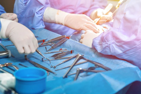 Sluiten van de handen van de arts tijdens de operatie in de operatiekamer. Steriele chirurgie instrumenten gebruikt in een echte operatie. Focus ligt op de rij klemgrepen. — Stockfoto