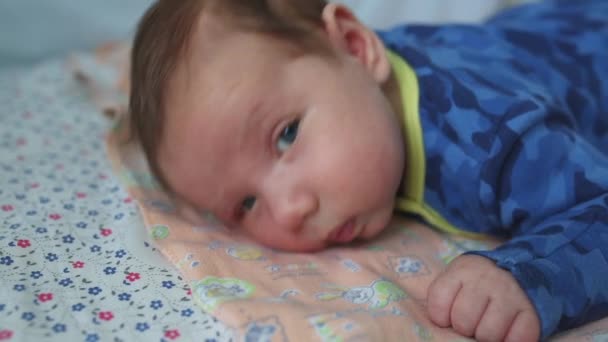 Criança encontra-se em seu estômago com grandes olhos abertos em uma cama para recém-nascidos . — Vídeo de Stock
