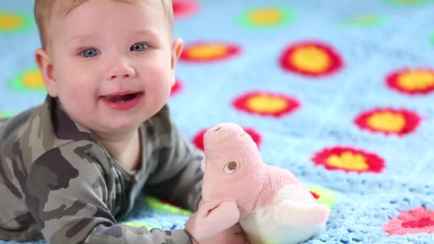 Hermoso bebé sonriente: Un bebé precioso se encuentra en la cama y sonríe a la cámara con un fondo de enfoque suave agradable — Vídeos de Stock