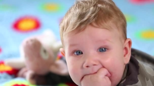 Hermoso bebé sonriente: Un bebé precioso se encuentra en la cama y sonríe a la cámara con un fondo de enfoque suave agradable — Vídeos de Stock