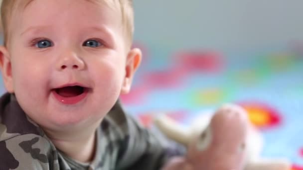 Gyönyörű mosolygós baba: egy gyönyörű kis baba fekszik az ágyon, és mosolyog a kamera egy szép puha fókusz háttér — Stock videók