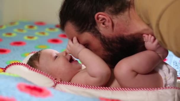 Der bärtige Vater spielt mit seinem Neugeborenen, das auf dem Bett liegt. Konzept Vater und Sohn. ein Mann und ein Neugeborenes. — Stockvideo