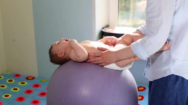 Mom does exercises for development with the baby on the fitball. Baby development concept, caring mom, toning exercises for babies — Stock Video