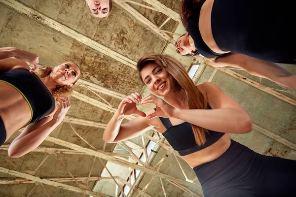 Groupe de jeunes filles sportives se reposant après une séance d'entraînement dans un studio loft spacieux. Amitié féminine dans la salle de gym, détente après remise en forme, intérieur, effet soleil éblouissant . — Photo