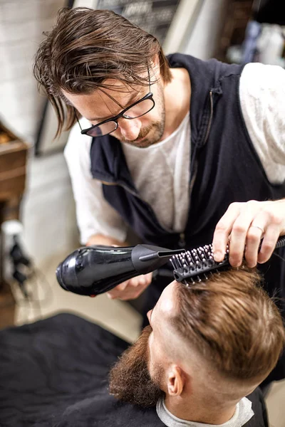 Mistrza tnie włosy i broda mężczyzn w salonie fryzjerskim, fryzjer sprawia, że fryzurę dla młodego człowieka — Zdjęcie stockowe
