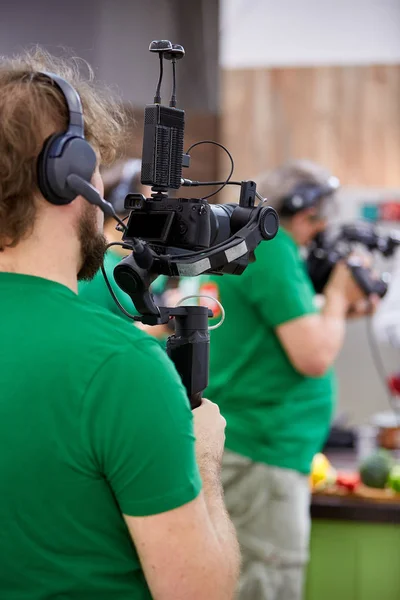 Videofilmer, der einen Film oder eine Fernsehsendung in einem Studio mit einer professionellen Kamera hinter der Bühne aufnimmt — Stockfoto