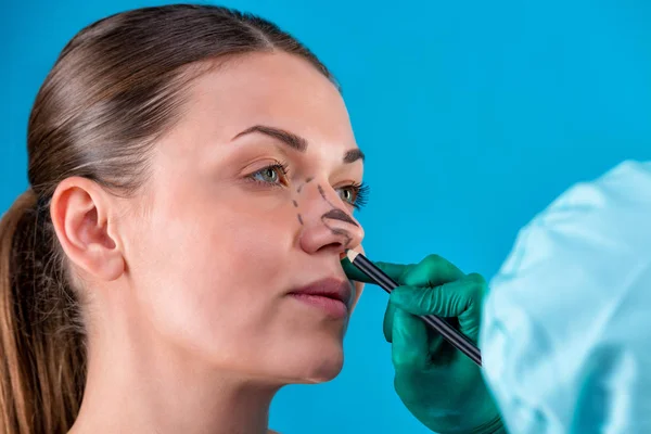 Beautician draw correction lines on woman face. Before plastic surgery operetion. Isolated on blue — Stock Photo, Image