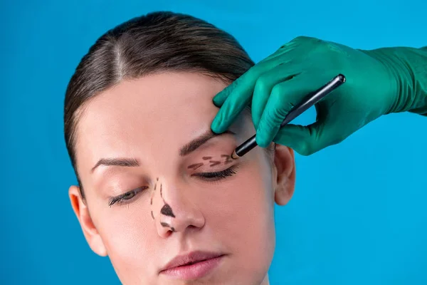 Beautician draw correction lines on woman face. Before plastic surgery operetion. Isolated on blue — Stock Photo, Image