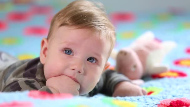 Hermoso bebé sonriente: Un bebé precioso se encuentra en la cama y sonríe a la cámara con un fondo de enfoque suave agradable — Vídeos de Stock