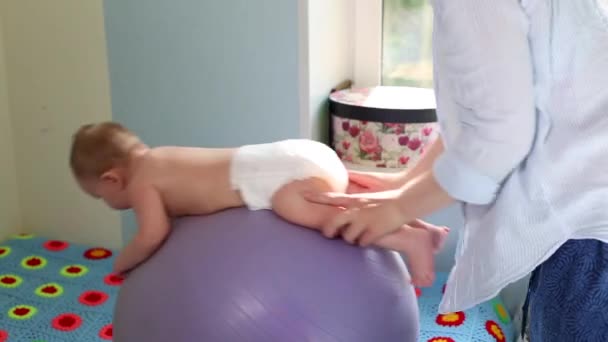 Äiti tekee harjoituksia kehitykseen vauvan kanssa kuntopallolla. Vauvan kehityksen käsite, huolehtiva äiti, vauvojen pehmentämisharjoitukset — kuvapankkivideo