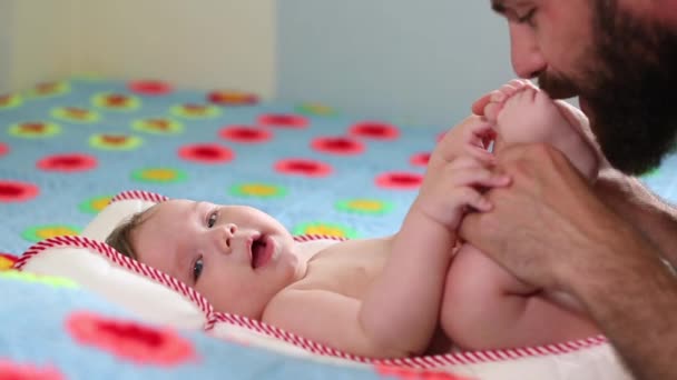 El padre barbudo Millennial juega con su hijo recién nacido acostado en la cama. Concepto padre e hijo. Un hombre y un recién nacido . — Vídeos de Stock