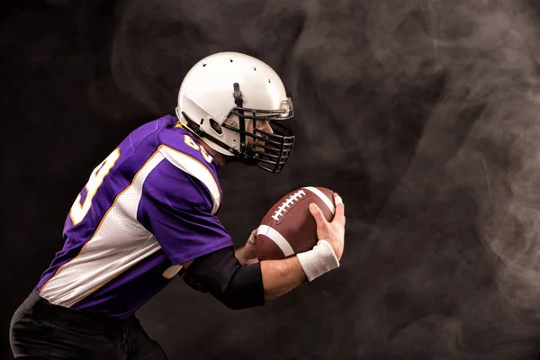 American football player holding the ball in his hands. Black background, copy space. The concept of American football, motivation, copy space