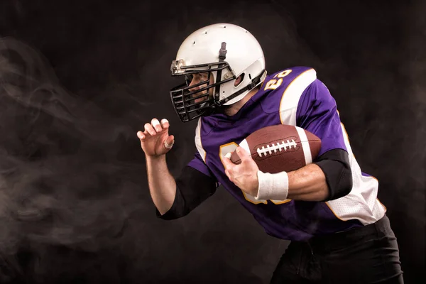 American football player holding the ball in his hands. Black background, copy space. The concept of American football, motivation, copy space