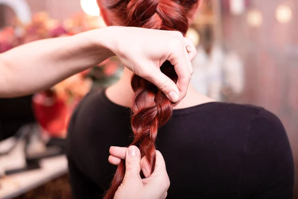 Hermosa chica pelirroja de pelo largo, peluquera teje una trenza francesa, en un salón de belleza. Cuidado profesional del cabello y la creación de peinados. — Foto de Stock