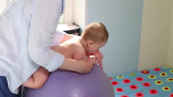 Η μαμά κάνει ασκήσεις για την ανάπτυξη με το μωρό στην μπάλα. Έννοια της ανάπτυξης μωρών, φροντίδα μαμά, τόνωση ασκήσεις για τα μωρά — Αρχείο Βίντεο