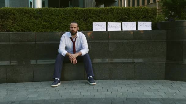 Desempleo, desempleado, despido, reducción de personal. Un hombre sin trabajo. Un joven se sienta en la calle con un cartel disparado, necesita un trabajo . — Vídeo de stock