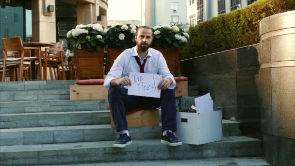 Arbetslöshet, arbetslös person, avskedande, downsizing. En man utan jobb. En ung man sitter på gatan med en skylt avfyras, behöver ett jobb. — Stockvideo