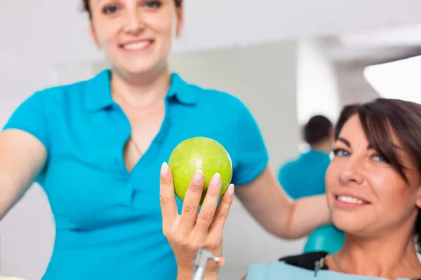 Dentistry, healthy teeth. Dentist gives green apple to a beautiful girl, a patient to check the teeth. Testing teeth with a green apple.