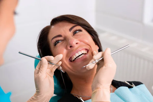 Ein Zahnarzt beendet eine erfolgreiche Zahnrestaurierung, ein Arzt berät eine glückliche Patientin, eine schöne langhaarige Frau betrachtet ihre sauberen, weißen, gesunden Zähne mit großer Freude — Stockfoto