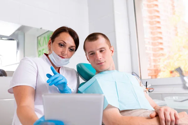 Dentist finishing successful teeth restoration, black haired doctor, in green mask, giving to happy patient mirror, beautiful long-haired woman looking at pristine white teeth with great pleasure — Stock Photo, Image