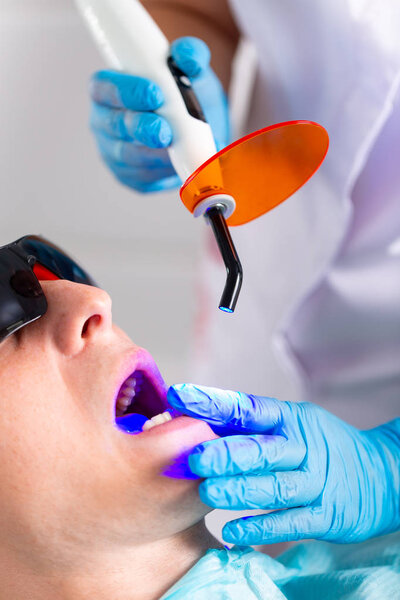 Close-up portrait of a male patient at dentist in the clinic. Teeth whitening procedure with ultraviolet light UV lamp.