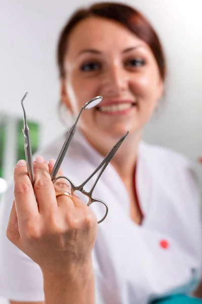 Mooie, lachende tandarts met gereedschap in de hand. Tandheelkunde, tandheelkundige behandeling, gezondheid. — Stockfoto