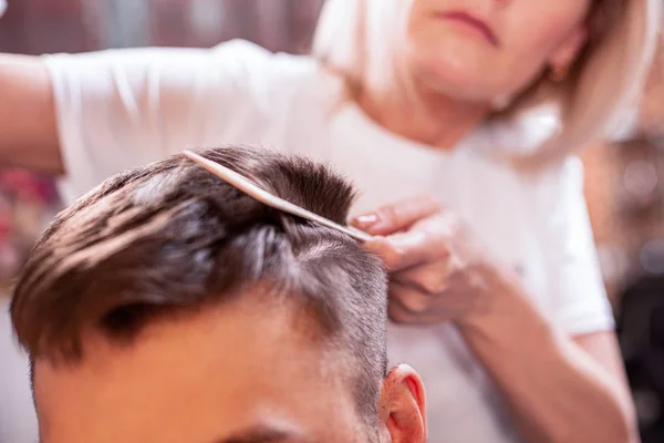 Der Meister legt die Haare eines Mannes in einen Friseursalon, ein Friseur fertigt mit Hilfe von Gel und Lack eine Frisur für einen jungen Mann an. — Stockfoto