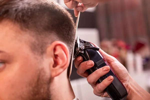 Der Meister schneidet einem Mann in einem Friseursalon die Haare und den Bart, ein Friseur schneidet einem jungen Mann die Haare. Schönheitskonzept, Selbstpflege. — Stockfoto